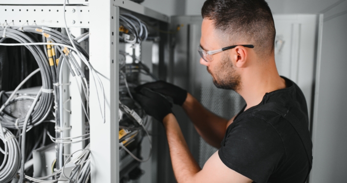 A technician works with server equipment in a data center. A man commutes wires in a server room