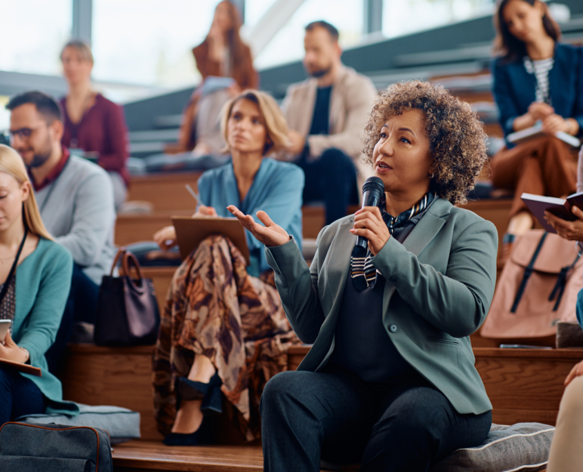 Mature businesswoman using microphone while speaking from audience during a seminar.